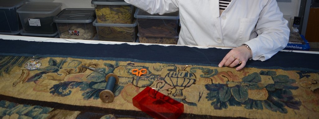 Mains d’une restauratrice au travail sur une bordure de tapisserie