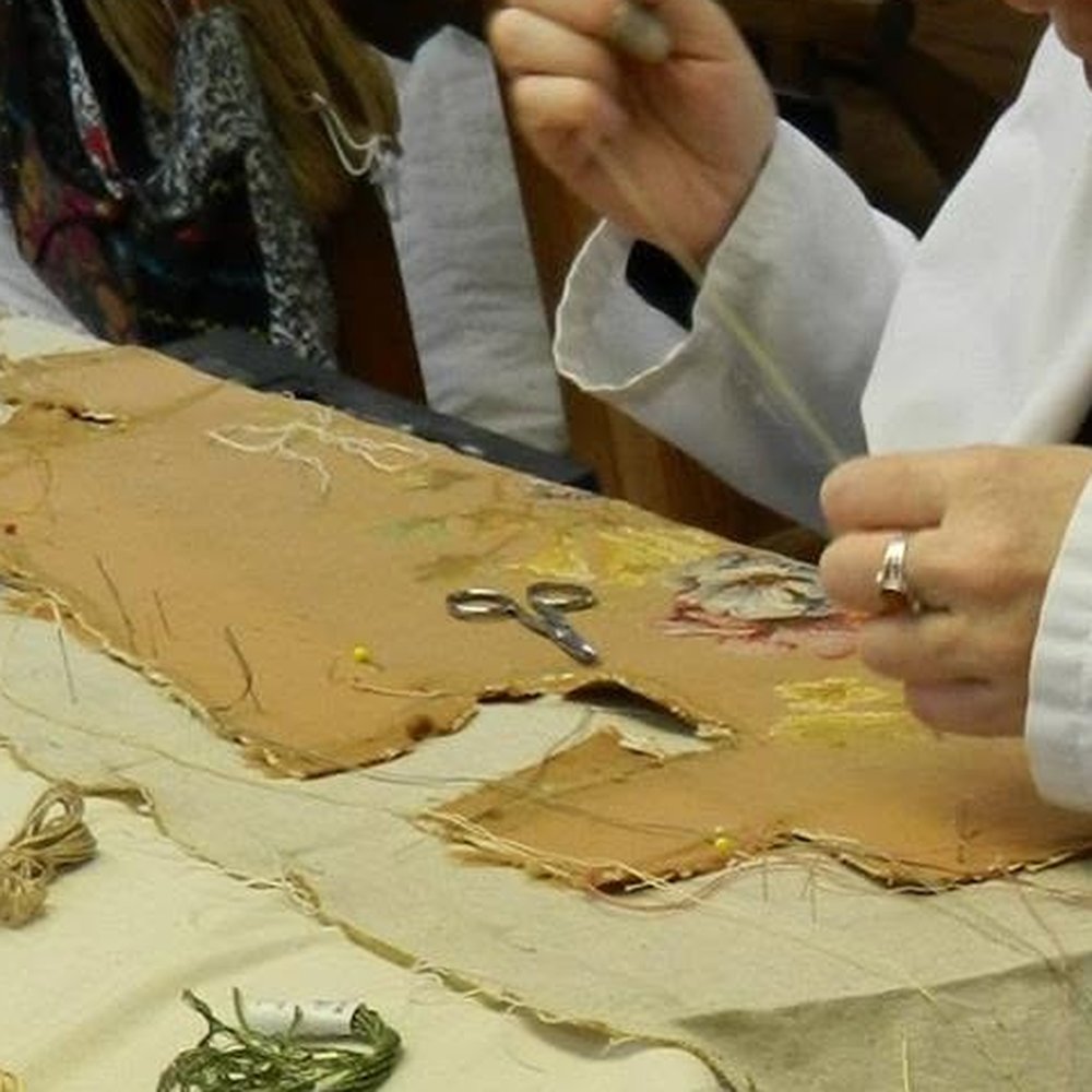 Mains d’une restauratrice tirant l’aiguille sur une tapisserie